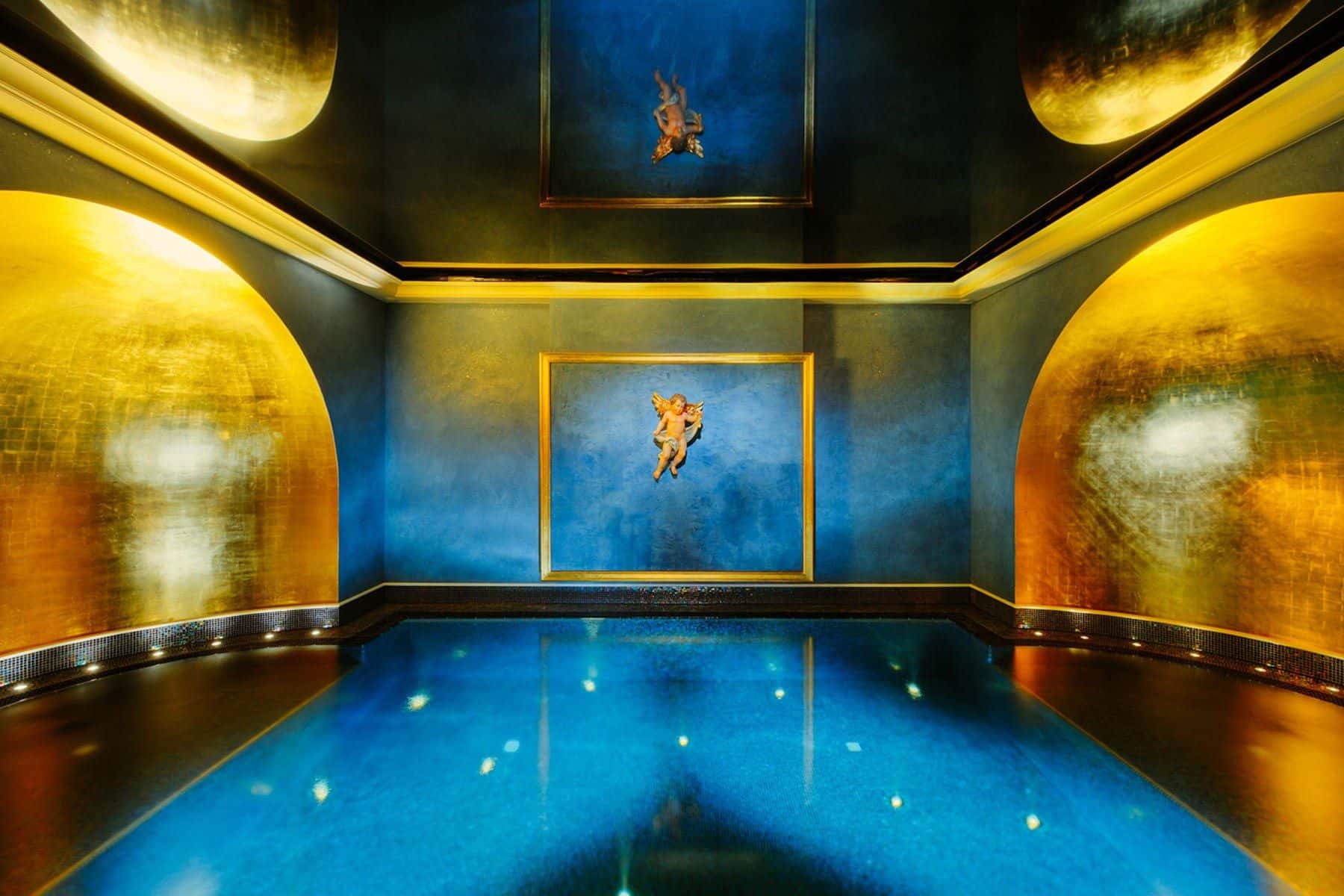 Blau beleuchteter Floating-Pool mit goldschimmernden Waenden, Engelsrelief und Gemaelde im Spa Wolke 7