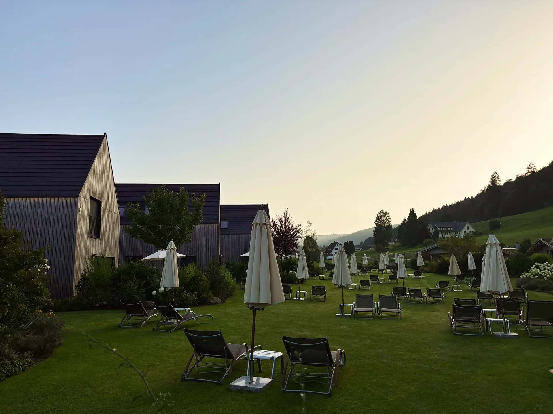 Liegewiese mit Sonnenschirmen und Liegestühlen vor Chalets in der Abenddämmerung.